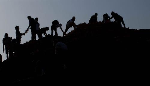 Photo shows people volunteering after a devastating earthquake in Nepal to recover bricks and heritage items from a destroyed temple in 2015. The volunteers, shown in silhouette, pass items hand to hand from the roof down to the ground.