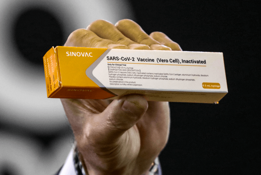 Sinovac vaccine Photograph of a hand holding a small yellow, grey and white box with the words “Sinovac,” “SARS-CoV-2 Vaccine” and “Inactivated” printed on it.